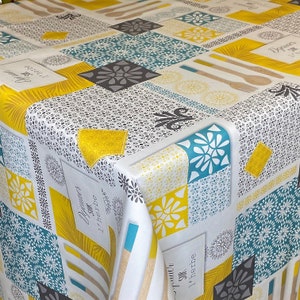 Può includere: Una tovaglia bianca con un motivo geometrico colorato con quadrati gialli, blu e grigi. Il motivo include fiori stilizzati e il testo "Diner sur l'herbe".