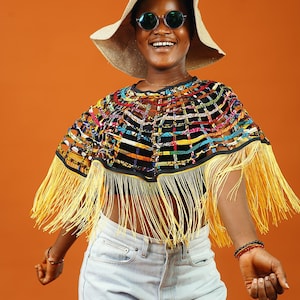 May include: A woman wearing a colorful, fringed poncho with a straw hat and round sunglasses. She is smiling and looking to the right.