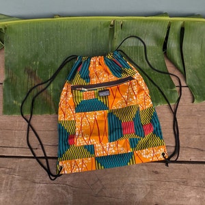 Può includere: Una borsa a cordoncino gialla, rossa, verde e blu con una tasca con cerniera. La borsa ha un motivo geometrico ed è realizzata in tessuto.