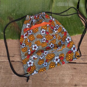 May include: A drawstring bag with a floral print. The bag is orange, white, and red with a small orange zippered pocket. The bag is made of fabric and has black drawstrings.