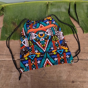 Può includere: Una borsa a sacco nera con un motivo geometrico colorato. La borsa ha una tasca con cerniera sul davanti e una zip arancione brillante. La borsa è realizzata in tessuto e ha una chiusura a coulisse.