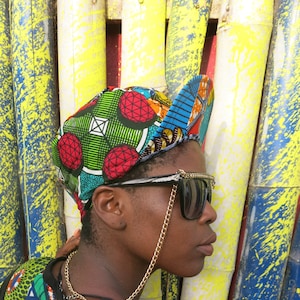 May include: A person wearing a colourful patterned baseball cap with a gold chain attached to sunglasses. The person is wearing a colourful patterned shirt with a black base.