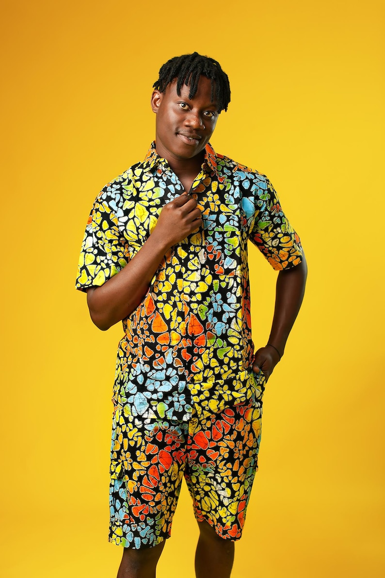 A man stands in front of a yellow background wearing Funky Men’s Cargo Shorts made from multicoloured African print fabric with a butterfly pattern in orange, yellow, blue, and black. The shorts have a relaxed fit and side pockets, paired with a matching short-sleeve shirt. This is a bold Summer Hawaiian Shorts look, ideal for African Print Men’s Clothing, a Hippie Festival Set, or a Carnival Outfit from Ashanti Empress.