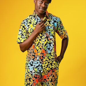 Op de afbeelding: Een persoon draagt ​​een shirt met korte mouwen en een bijpassende short met een kleurrijke abstracte print. Het shirt heeft een knoopsluiting en de short heeft een ontspannen pasvorm. De persoon staat tegen een gele achtergrond.