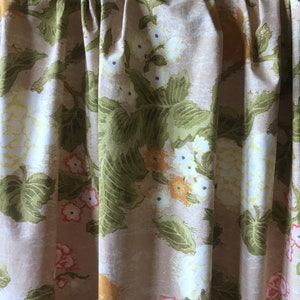 Könnte beinhalten: Ein beigefarbener Stoff mit einem floralen Muster aus grünen Blättern, weißen Blüten und orangefarbenen und rosafarbenen Akzenten.