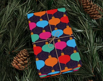May include: A wrapped gift with colorful ornament pattern on a dark purple background, tied with twine. The ornaments are red, orange, blue, green, and pink. The gift is surrounded by pine needles and pine cones.