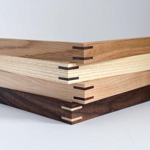 May include: Four wooden picture frames with mitered corners and a dark wood inlay. The frames are stacked on top of each other, with the largest frame on the bottom and the smallest frame on top.