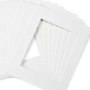 May include: A stack of white mat boards with a cut-out opening in the center. The mat boards are designed for framing photos or artwork.