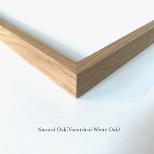 May include: Close-up of a corner of a natural oak picture frame. The frame is made of solid wood and has a smooth finish. The text "Natural Oak (Varnished White Oak)" is visible below the frame.