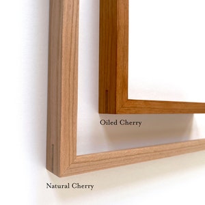 May include: Two wooden picture frames, one in natural cherry and one in oiled cherry. The frames are both made of solid wood and have a simple, elegant design.