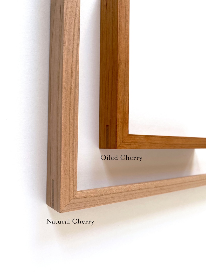 May include: Two wooden picture frames, one in natural cherry and one in oiled cherry. The frames are both made of solid wood and have a simple, elegant design.
