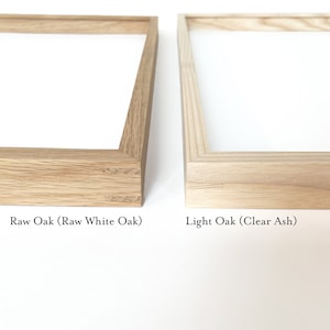 May include: Two wood picture frames, one with a raw oak finish and the other with a light oak finish. The text "Raw Oak (Raw White Oak)" is below the first frame and the text "Light Oak (Clear Ash)" is below the second frame.