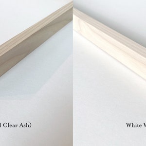 May include: Close-up of two wood picture frames, one with a natural light oak finish and the other with a white wash light oak finish. Both frames are made of clear ash wood.