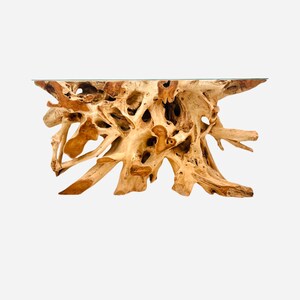 May include: A large, natural wood console table with a unique, organic shape and a clear glass top. The table is made from a single piece of wood, and the knots and grain patterns are visible.