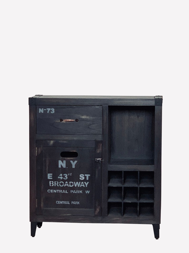 May include: Dark gray wooden cabinet with a drawer, door, and wine rack. The cabinet has the text "N.Y. E 43rd ST BROADWAY CENTRAL PARK W CENTRAL PARK" printed on the door. The drawer is labeled "N-73".
