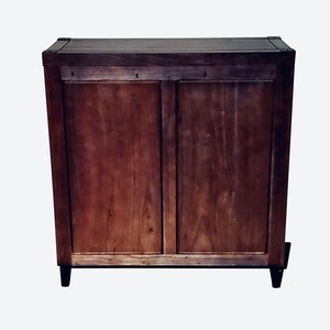 May include: A wooden cabinet with a dark brown finish. The cabinet has two doors and sits on four black legs. The wood grain is visible, and the cabinet appears to be well-constructed.