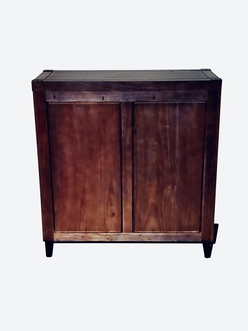 May include: A wooden cabinet with a dark brown finish. The cabinet has two doors and sits on four black legs. The wood grain is visible, and the cabinet appears to be well-constructed.