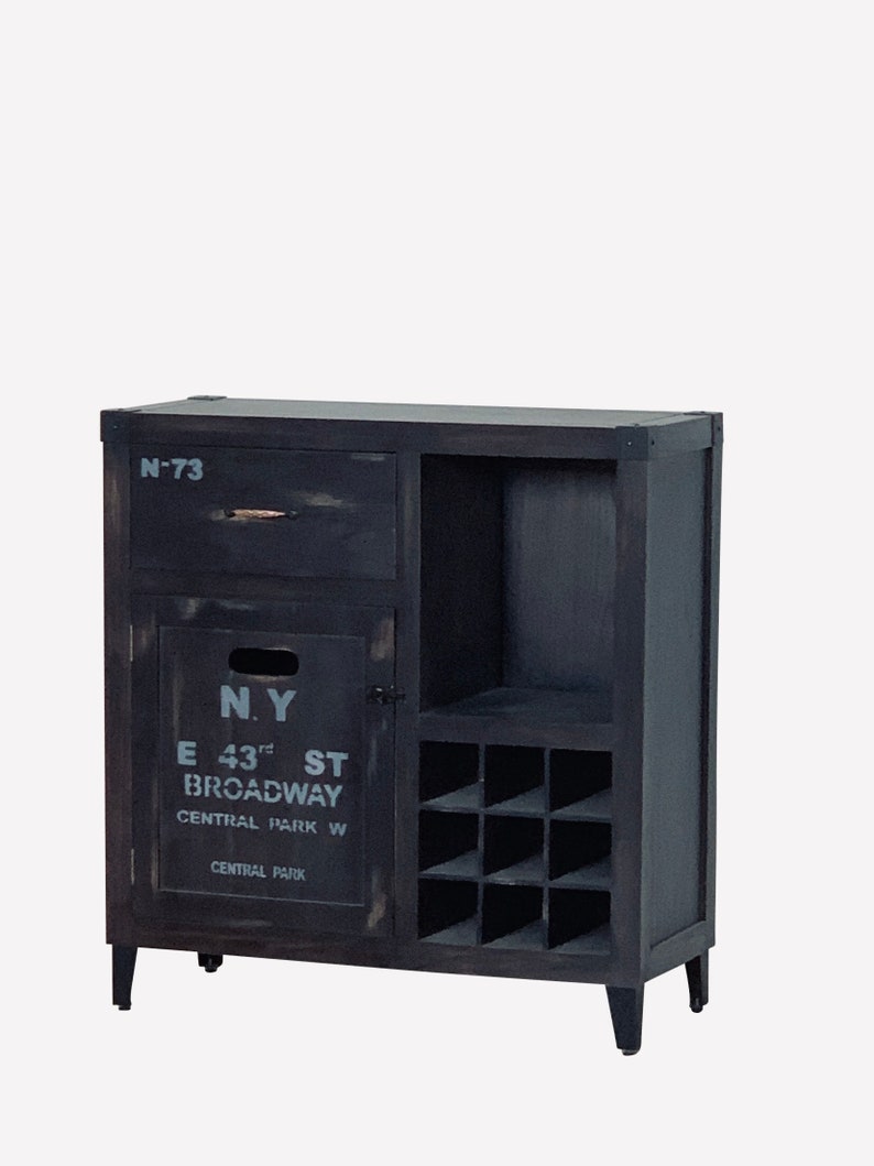 May include: A distressed black wooden cabinet with a drawer, a door with the text "N.Y E 43rd ST BROADWAY CENTRAL PARK W CENTRAL PARK", and a wine rack. The cabinet has four short legs and a dark finish.