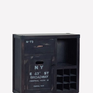 May include: A dark-stained wooden cabinet with a drawer, a door, and a wine rack. The door features the text "N.Y. E 43rd ST BROADWAY CENTRAL PARK W CENTRAL PARK" in white. The cabinet has four black legs.