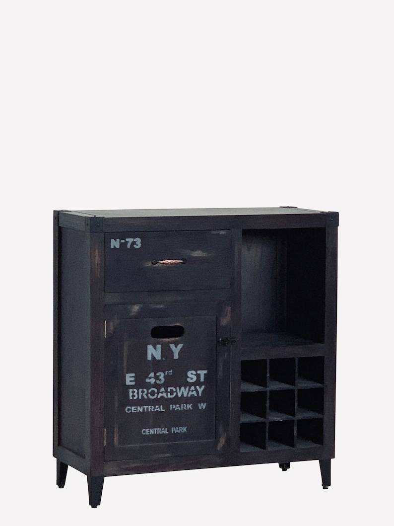 May include: A dark-stained wooden cabinet with a drawer, a door, and a wine rack. The door features the text "N.Y. E 43rd ST BROADWAY CENTRAL PARK W CENTRAL PARK" in white. The cabinet has four black legs.