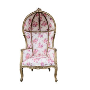 May include: A vintage-style chair with a pink floral patterned fabric upholstery and a canopy top. The chair has a carved wooden frame and ornate legs.