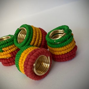 May include: Five colorful hair rings with a gold metal core. Each ring is made of three bands of yarn in red, yellow, and green.
