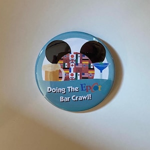 May include: A round, blue button with a Mickey Mouse head design. The button features a beer mug and a cocktail glass. The center of the button has a collage of international flags. Text on the button reads "Doing The Epcot Bar Crawl!"