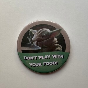 May include: A round button featuring a green and brown design with the text "DON'T PLAY WITH YOUR FOOD!". The image shows a character from a popular science fiction series.