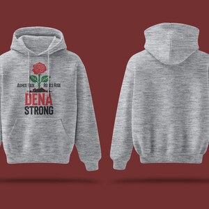 May include: A gray hooded sweatshirt with the text "Ashes Fade, Roses Rise" and "Dena Strong" printed on the front. A red rose with green leaves is printed above the text.