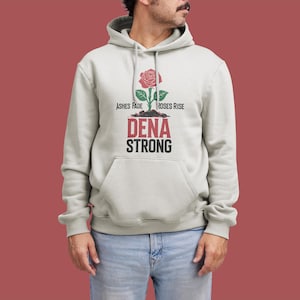 K&ouml;nnte beinhalten: Ein hellgrauer Hoodie mit einem Rosenmotiv und dem Text "Ashes Fade Roses Rise Dena Strong".