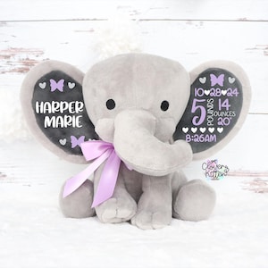 May include: A gray plush elephant with a lavender bow. The elephant's ears have black accents with white text that reads "HARPER MARIE" and birth details: 5 pounds, 14 ounces, and 20 inches. The ears also feature purple butterflies.