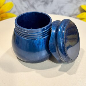 May include: A small, round, blue wooden box with a lid. The box has a smooth, glossy finish and is made of wood with a blue stain.