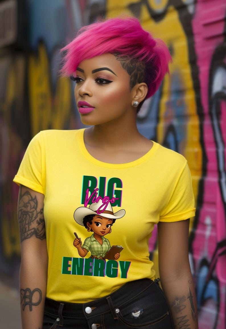 May include: A yellow t-shirt with the words "BIG Virgo ENERGY" and a cartoon cowgirl graphic. The person in the image has pink hair and is wearing black jeans. The background is a colorful graffiti wall.