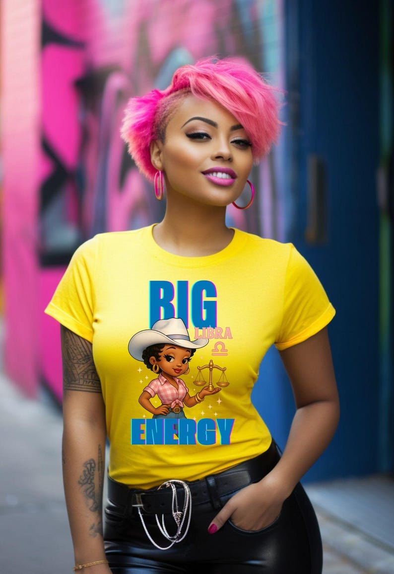 May include: Yellow t-shirt with the words "BIG ENERGY" and a Libra graphic. The graphic features a cartoon woman wearing a cowboy hat and holding scales. The woman in the image has pink hair and hoop earrings.