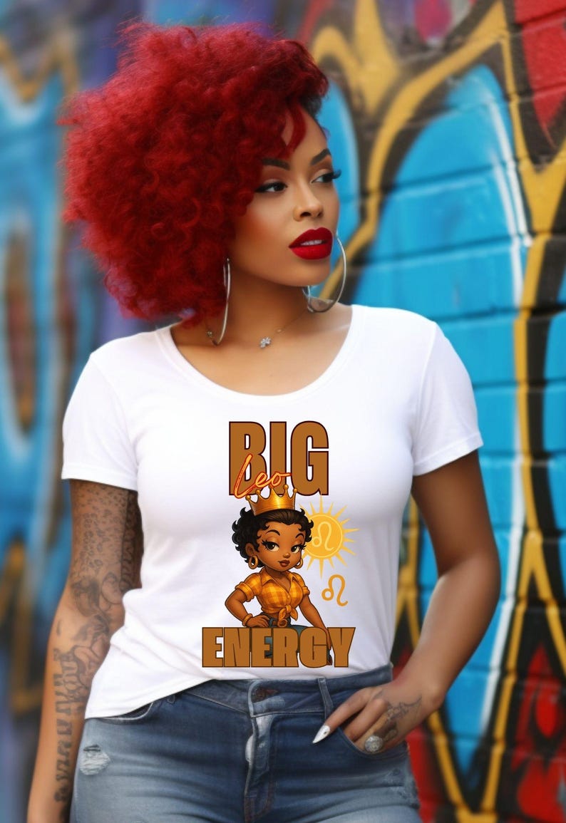 May include: White t-shirt with the text "BIG Leo ENERGY" and a cartoon illustration of a woman wearing a crown. The woman has dark skin and is wearing a gold-colored top. The background is a colorful graffiti wall.