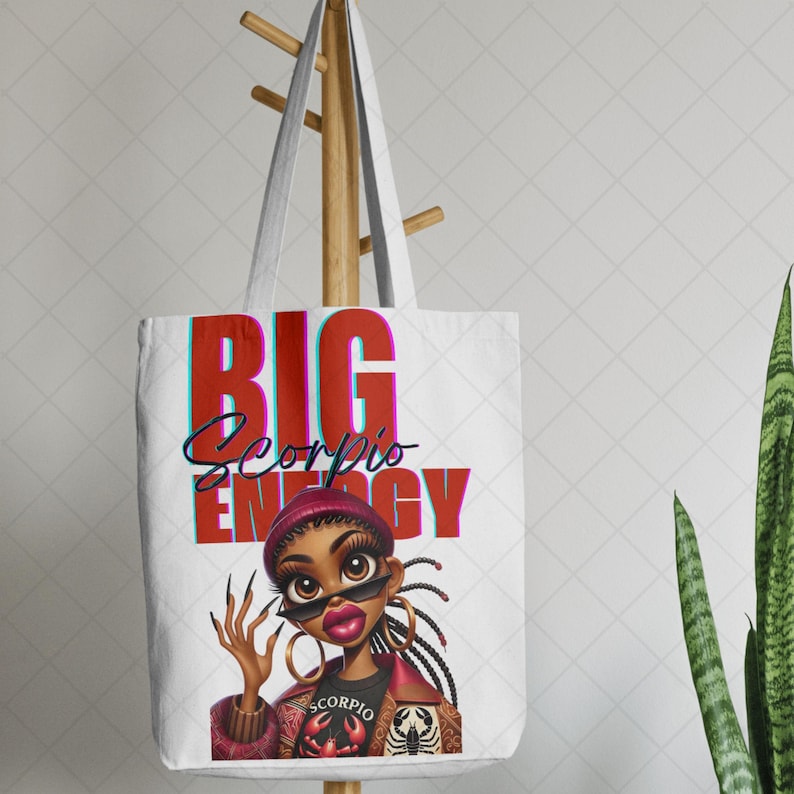 May include: White tote bag with the words "BIG Scorpio ENERGY" in red and teal. The bag features a cartoon illustration of a woman wearing sunglasses, a burgundy hat, and a black shirt with a scorpion graphic.