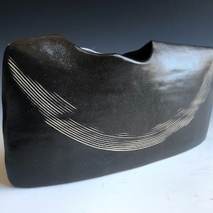 May include: Black ceramic vase with a white, curved line design. The vase has a unique, organic shape.