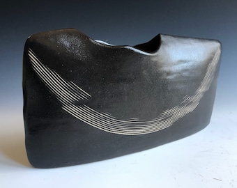 May include: Black ceramic vase with a white, curved line design. The vase has a unique, organic shape.