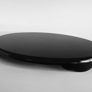 May include: A black oval-shaped ceramic stand with a smooth, glossy finish. The stand has three small feet on the bottom.