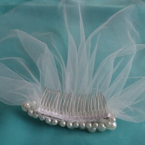 May include: A white tulle bridal veil with a comb and pearl embellishments.