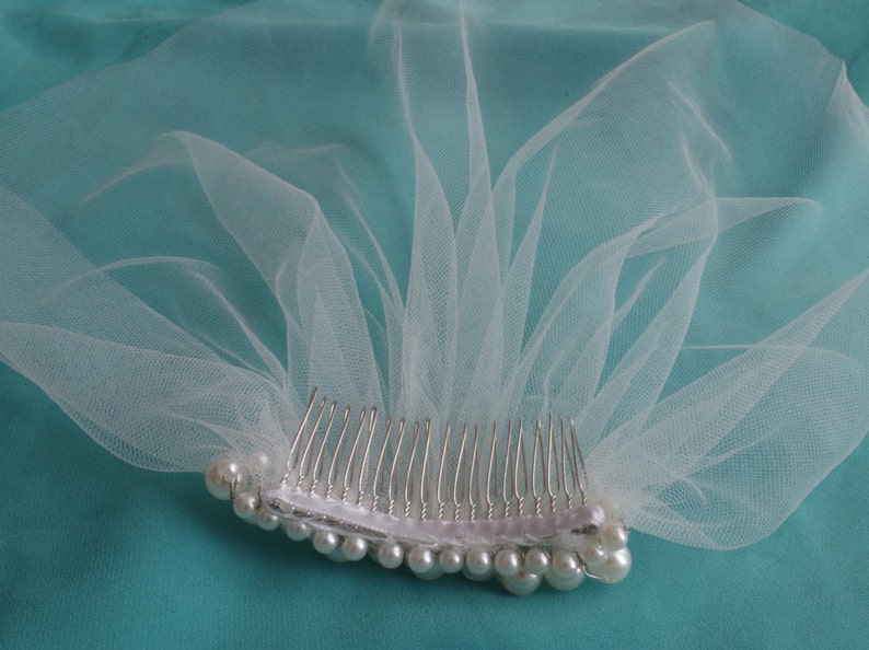 May include: A white tulle bridal veil with a comb and pearl embellishments.