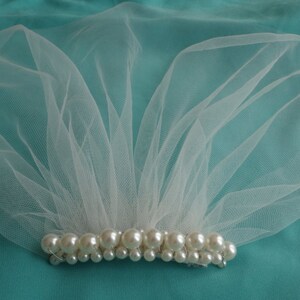 May include: A white tulle veil with a row of pearl beads along the bottom edge.