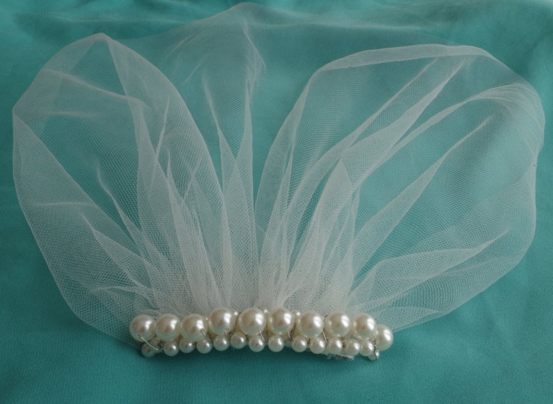 May include: A white tulle veil with a row of pearl beads along the bottom edge.
