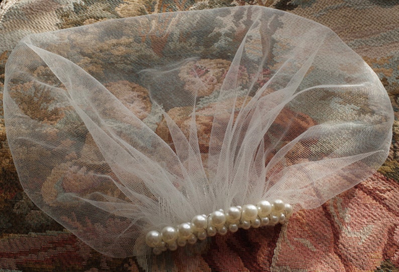 May include: A white tulle veil with a row of pearl beads sewn across the bottom edge.