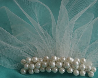 Peut inclure: Un voile en tulle blanc avec un groupe de perles blanches attachées au bord inférieur.