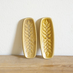 Può includere: Due piccole ciotole rettangolari in ceramica con un motivo a foglie. Le ciotole sono di colore giallo chiaro con un motivo a foglie giallo scuro.