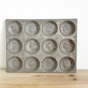 Pode incluir: Uma forma de assar de metal vintage com 12 moldes individuais. Cada molde tem um design diferente: um coração, um diamante, um paus e um trevo. A forma está ligeiramente enferrujada e mostra sinais de idade.