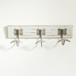 May include: A white wooden coat rack with three metal hooks. The hooks are shaped like a crescent moon and have a rustic, aged look.