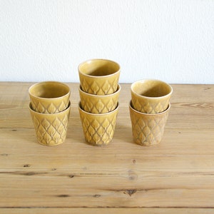 以下が含まれることがあります： 葉の模様が入った、黄色いセラミックカップ6個セット。木製の表面に積み重ねられています。各カップの高さは約7.6cm、直径は約7.6cmです。