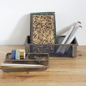 Könnte beinhalten: Zwei Schreibtisch-Organizer aus Metallgitter auf einer Holzoberfläche. Einer enthält Bücher und Marker, der andere Washi-Tape und Stifte. Die Organizer sind rechteckig mit dunklem, gealtertem Finish.